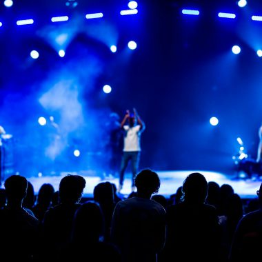 Vibrant live concert scene with audience silhouettes, stage performers, and dynamic lighting.