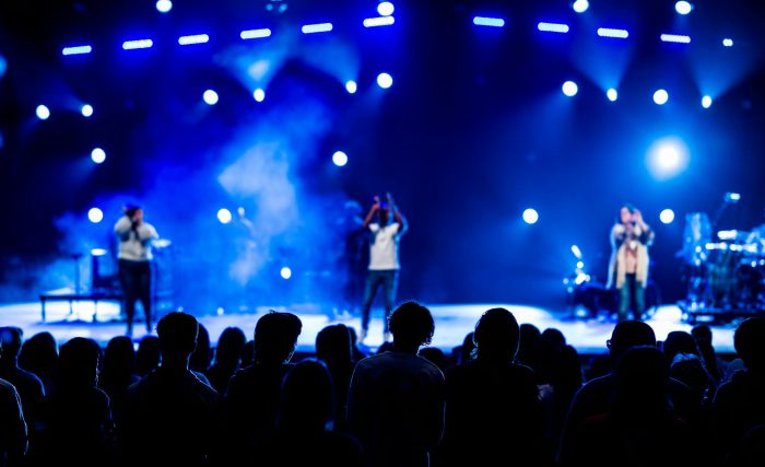 Vibrant live concert scene with audience silhouettes, stage performers, and dynamic lighting.